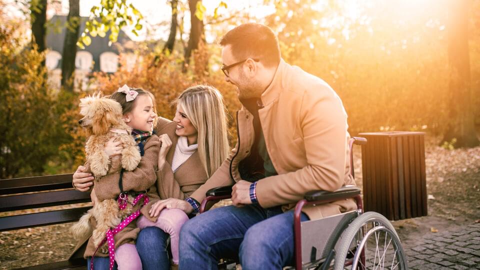 Family sitting outside on a park bench with a dog